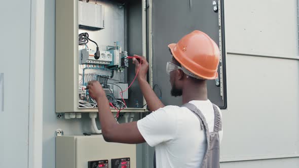 African American Electrician in Uniform and Helmet Standing Near Box with Cables alt