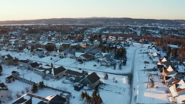 Picturesque winter aerial flying over a snowy suburban neighborhood at dusk. alt