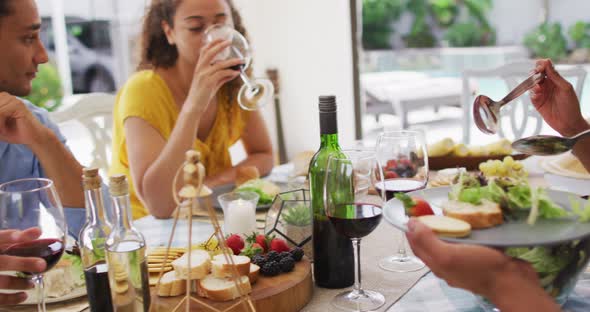 Group of diverse male and female friends drinking wine and talking at dinner party on patio alt