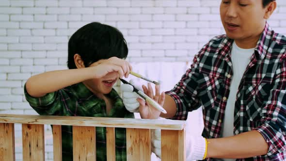 Young male carpenter teaching his son how to work with wood in workshop. alt