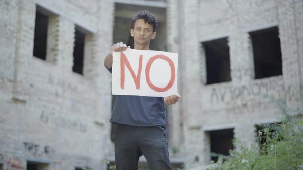 Portrait of Mixed-race Young Man Raising No Poster and Looking at Camera. Rack Focus Changes From alt