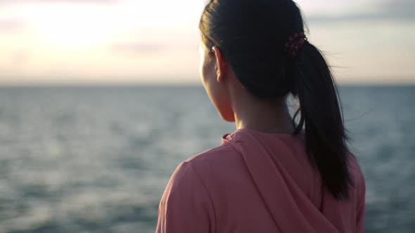 Woman runner standing seaside taking a break from exercising admiring the view of the beach sunset. alt