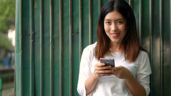 Young Asian women using smartphones send text messages at a public park.