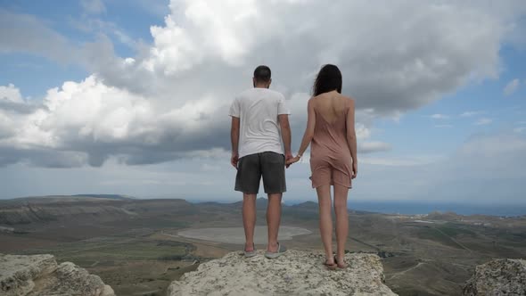 A Young Couple Stands on Top of a Mountain Holding Hands