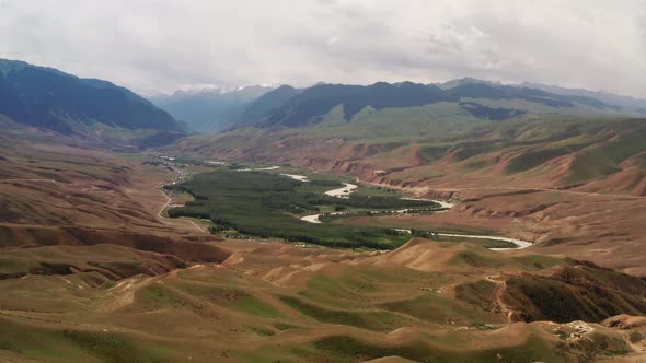 Mountain peaks and grassland are under white clouds alt