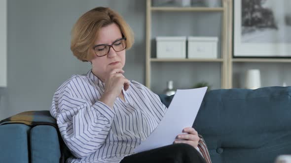 Pensive Old Woman Reading Agreement Sitting on Sofa alt