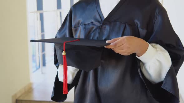 Indian Female Graduate in Mantle Stands with a Hat in Her Hands alt