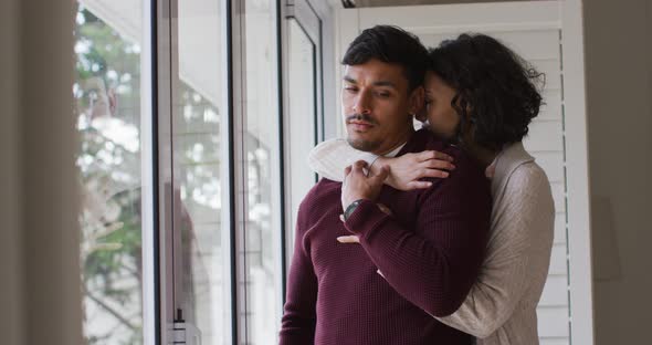 Romantic hispanic couple embracing cuddling standing in window alt