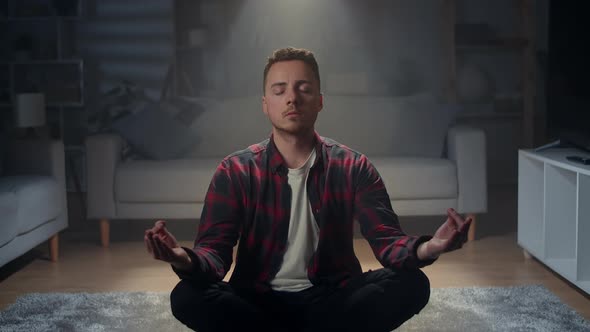 A Young Man Sits at Home on the Floor in the Lotus Position at Night