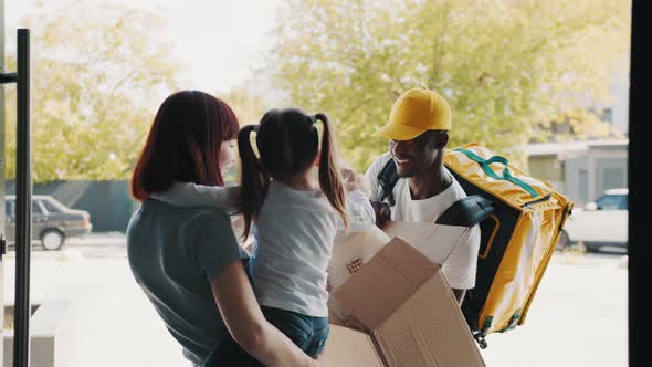 The Courier Brings a Parcel for a Little Girl with Her Mother at the Door of the alt