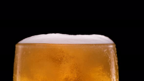 Light Beer Pouring in Glass with Bubbles and Foam on Black Background