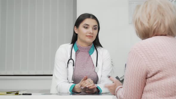 Young Female Doctor Listening To Her Senior Patient During Medical Appointment