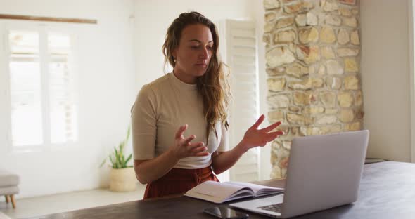 Smiling caucasian woman working from home making video call using laptop, talking and gesturing alt