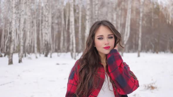 Young Woman with Wavy Hair Standing and Touching Face in Winter Forest