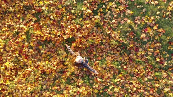 Top View Happy Cute Girl in Autumn Coat Takes and Throws Yellow Fallen Foliage alt