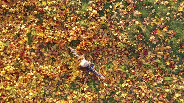 Top View Happy Cute Girl in Autumn Coat Takes and Throws Yellow Fallen Foliage