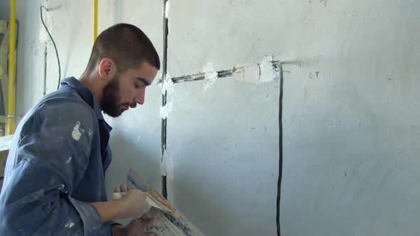 Bearded Contractor Spreading Plaster on Wire Trunking