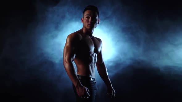 Asian Bodybuilder Man Demonstrates His Body, Strength and Endurance. Black Smoke Background alt