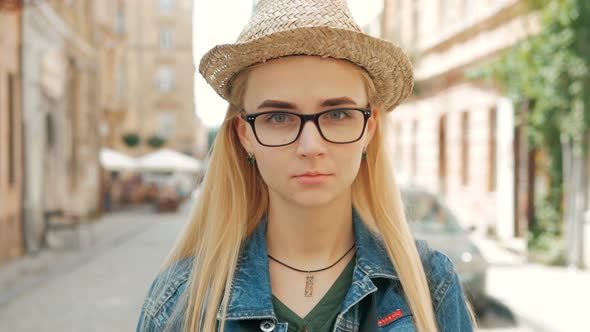 portrait of a beautiful blond girl with glasses, a hat and a blue jeans jacket.