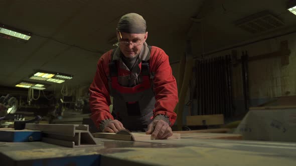 Carpenter Worker Cuts a Wooden Board with a Circular Saw on a Workbench