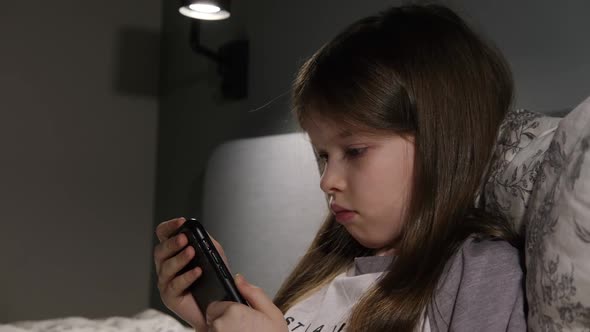 Little Girl Sitting with a Smartphone at Night Games Online Learning alt