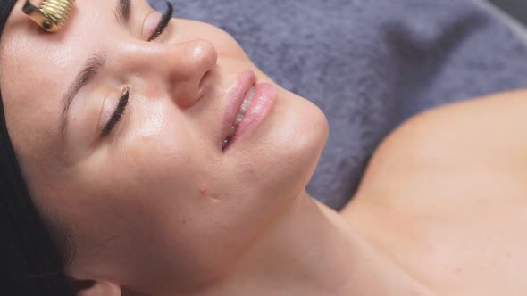 Facial Massage the Cosmetologist Uses a Derma Roller To Lift and Tighten the Skin of the Face alt