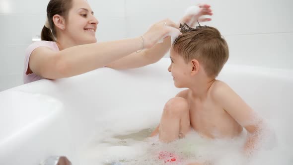 Happy Smiling Mother Playing with Her Son Washing in Bath with Soap Foam alt