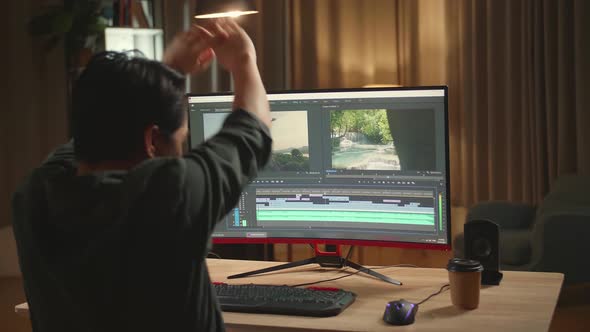 Asian Male Video Editor Stretching While Works With Footage And Sound On His Personal Computer alt