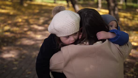 Happy Little Children Cuddling with Mother in Park alt