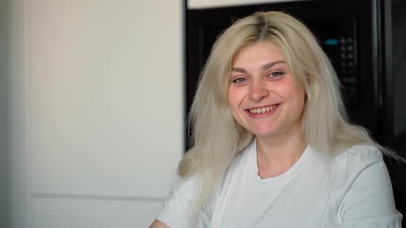 Confident smiling young adult european woman looking at camera sitting at home kitchen