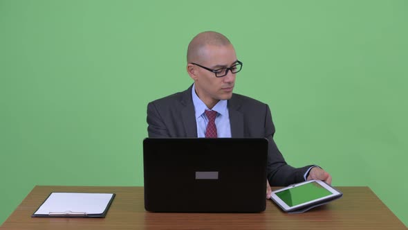 Busy Bald Multi Ethnic Businessman Multitasking at Work Behind Desk alt