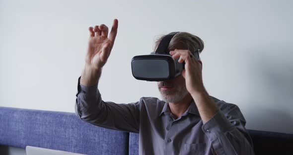 Caucasian businessman sitting on couch using vr googles in office alt