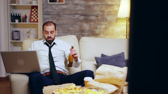 Businessman Reaching Out for His Beer While Working on Laptop alt