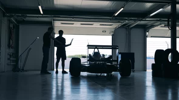 Two Professionals are Looking at the Racing Car in the Workshop alt