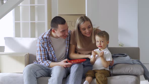 Happy Family Couple with Kid Son Eating Snacks on Moving Day in New Home alt
