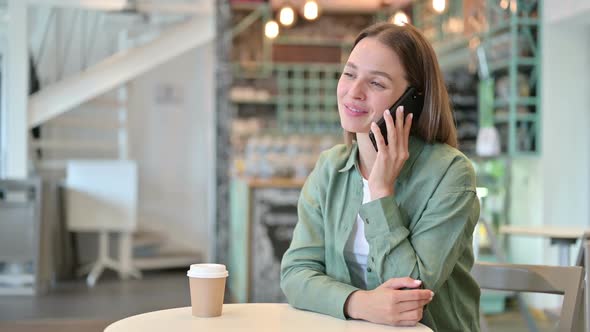 Cheerful Young Woman Talking on Smartphone in Cafe alt