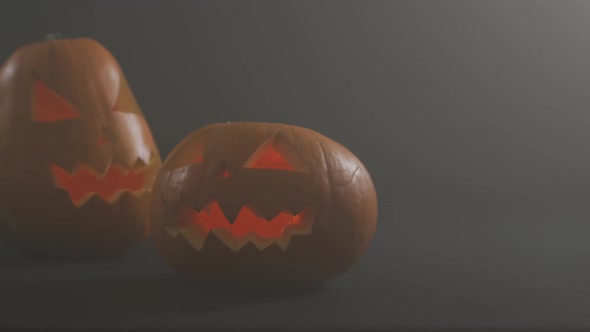 Smoke effect over two scary face carved halloween pumpkin against grey background alt