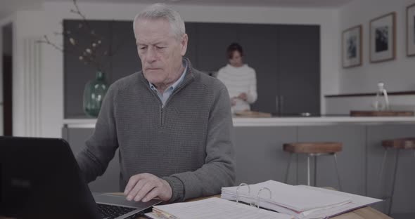 Senior adult male doing domestic finance on laptop at kitchen table, day in life