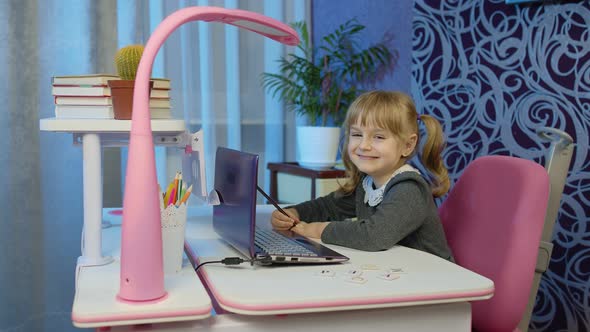 Child Girl Pupil with Textbook Doing School Homework Online Using Laptop Computer Smiling at Home alt