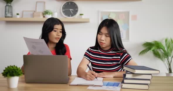Portrait of Two Asian schoolgirl studying online making notes in copybook alt
