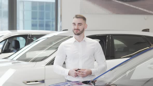 Handsome Happy Man Smiling to the Camera Standing at Car Dealership alt