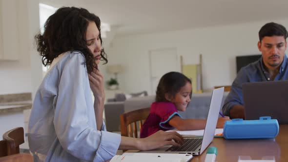 Hispanic parents sitting at table working with laptops and daughter drawing alt