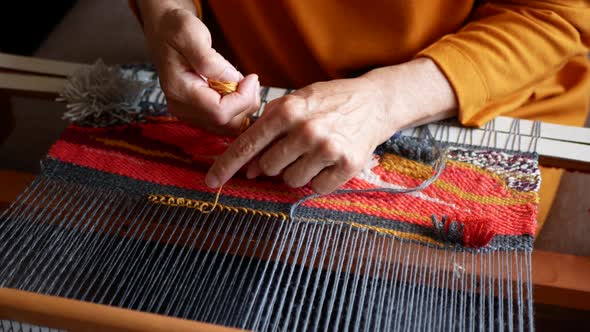 Women's hands using a loom to create a bright tapestry