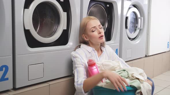 A Woman is Sitting on the Floor of the Laundry Room Next to the Washing Machines She is Very Tired