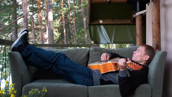 Man Playing Guitar on Sofa Outside Glamping Tent alt
