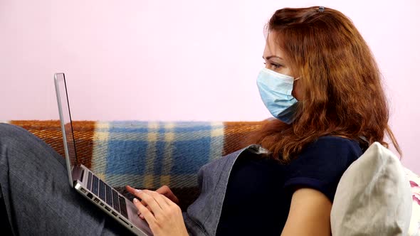  A Young Woman Works at Home at the Laptop in Medical Mask During Quarantine. Social Distancing