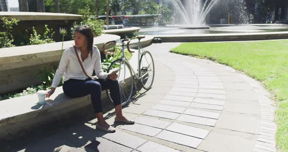 African american woman using smartphone drinking coffee in city park alt
