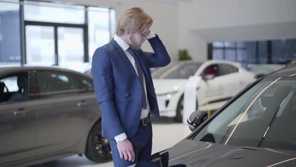 Bearded Businessman Choosing Car in Dealership Close Up. Tall Man Running Hand Through Hair Near alt