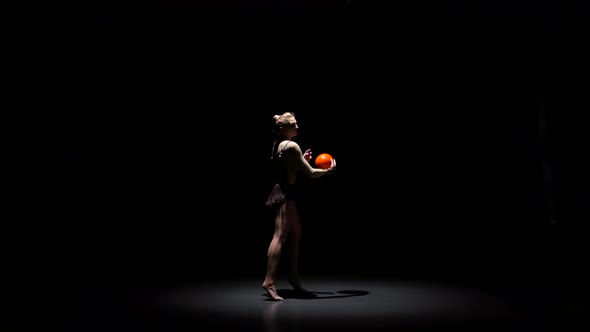 Gymnast with the Ball in His Hands Doing Acrobatic Moves. Black Background alt