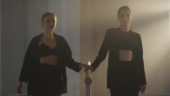 Medium Shot of Two Gorgeous Ballerinas Walking to Camera Along Barres and Looking at Each Other alt